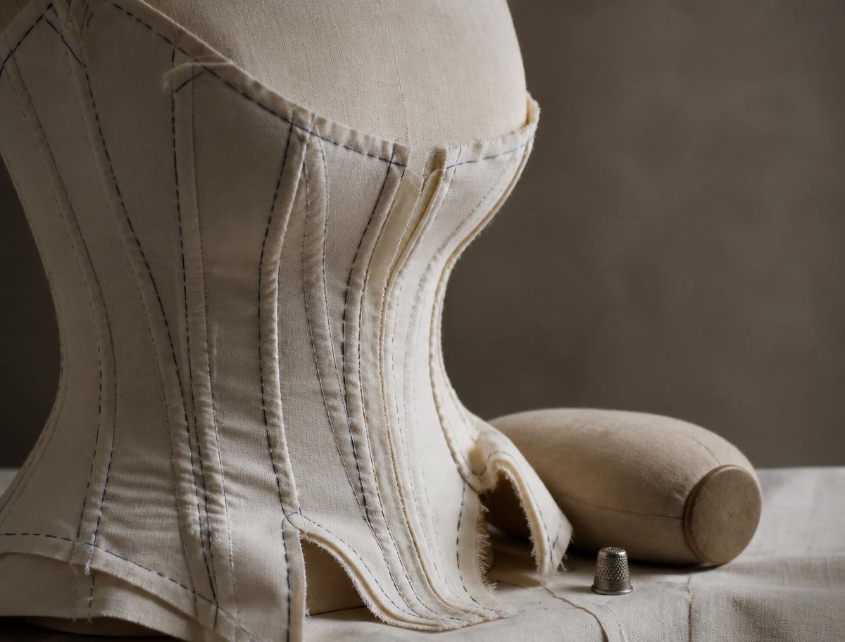 A hand-basted calico corset toile with boning channels beside a tailor's ham